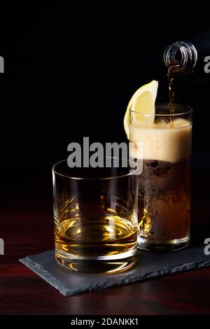 Whiskey ordentlich und Cola mit Eis und Zitronenkeil serviert auf Schieferplatte. Dunkelroter Holztisch, hohe Auflösung Stockfoto