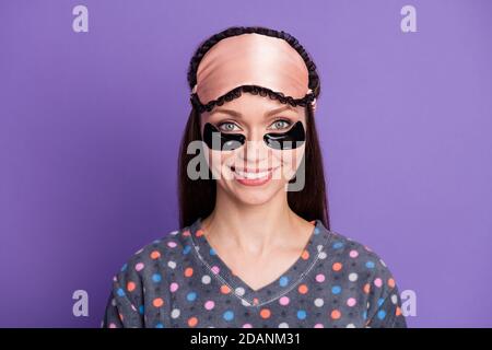 Foto von positiven fröhlichen Mädchen mit schwarzen Augen Flecken aussehen Gute Laune in der Kamera Genießen Sie weichen gesunden Schlaf tragen punktiert Pyjama Maske isoliert über violett Stockfoto