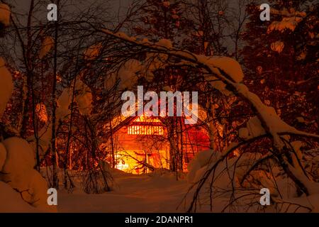 Winter Finnland. Dichter Wald und viel Schnee. Kleines Holzhaus und Nachtbeleuchtung Stockfoto