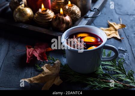 Glühwein mit Orange, Zimt und Anis im Becher mit Weihnachtsschmuck und Kerzen Stockfoto