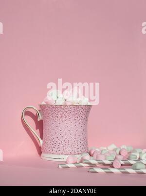 Tasse mit heißem Kakao und Marshmallows auf der Oberseite. Festliche heiße Getränk Rosa Hintergrund. Pinkfarbener Becher. Papier niedlichen Strohhalme für Getränke und zarte Marshmallow Würfel. Stockfoto