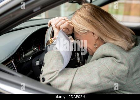 Verzweifelte reife blonde Geschäftsfrau mit Papier setzen ihren Kopf auf Steuern Stockfoto