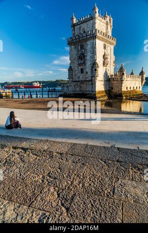 Ein Mädchen, das vor dem Belem Tower sitzt und darüber spricht Das Telefon und entspannend Stockfoto