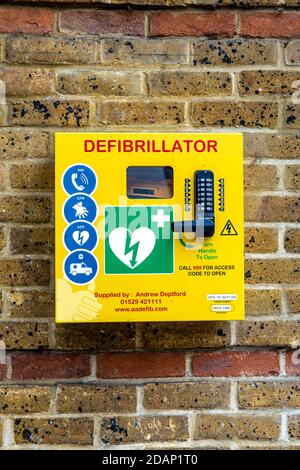 Gelbe Defibrillatorbox an einer Ziegelwand, Rickmansworth, Großbritannien Stockfoto