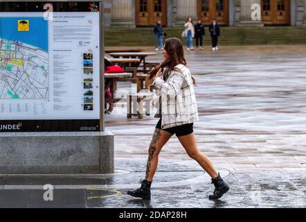 Dundee, Tayside, Schottland, Großbritannien. November 2020. UK News Covid-19 Lockdown. Menschen, die in Dundee auf den Straßen herumlaufen und nur wenige wichtige Bekleidungsgeschäfte geöffnet haben, da die strengere Stufe 3 Covid-19 Lockdown-Beschränkung durchgesetzt wurde. Eine große modische Frau mit markanten Tätowierungen auf ihrem rechten Bein ist sich der sozialen Distanzierungsrichtlinien bewusst, die im Stadtzentrum mit einer kleinen Tasse Kaffee an einem kalten und nassen November-Nachmittag gehen. Kredit: Dundee Photographics/Alamy Live Nachrichten Stockfoto