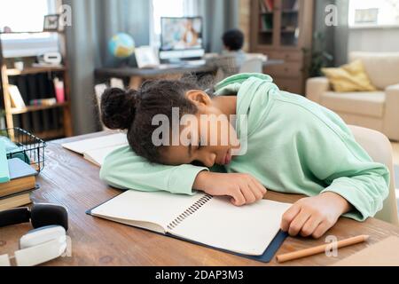 Müde gemischt-Rennen Schulmädchen in Casualwear liegen auf offenem Copybook auf Tabelle Stockfoto