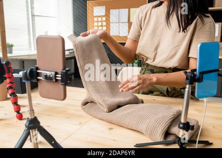 Junge Frau mit neuem gestrickten beigefarbenen Pullover vor Smartphone-Kamera Stockfoto