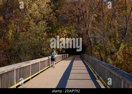 Ein Jogger überprüft sein Handy am Eingang zum Theodore Roosevelt Park, der von einem Fußgängerweg über den Potomac-Fluss erreicht wird. In Rosslyn, Ar Stockfoto