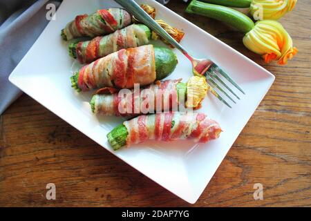 Gegrillte Zucchini-Pommes in einem Speck auf weißem Teller gewickelt Stockfoto