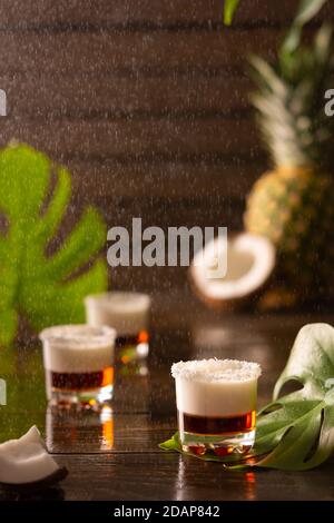 Tropische alkoholische Aufnahmen mit Kokosflocken, Monstera Blume mit Kokosnuss und Ananas auf braunem Holzhintergrund dekoriert Stockfoto