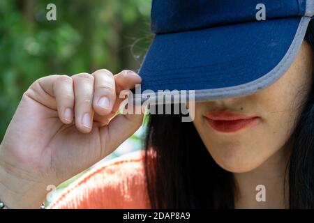 Frau versteckt ihr Gesicht hinter einer blauen Basecap Stockfoto