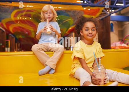 Zwei kleine Freunde trinken Milchcocktails, während sie sich nach Spielen ausruhen Im Play Center Stockfoto