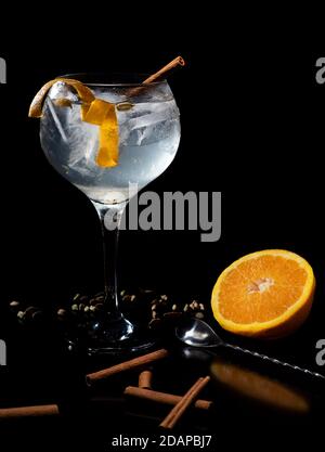 Gintonic mit Zimt und Orange auf schwarzem Hintergrund und Mit dem Spirallöffel und Kardamom Dekoration Stockfoto