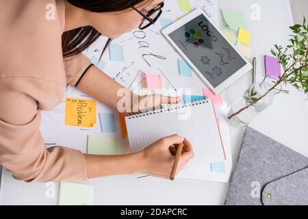 Junge Designerin macht Notizen im Copybook beim Biegen über Dokumente Stockfoto