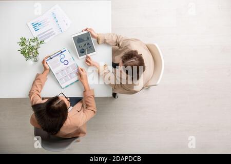Überblick über zwei junge elegante Geschäftsfrauen, die am Schreibtisch sitzen und Daten analysieren Stockfoto