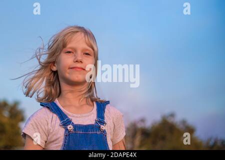 Portrait eines Mädchens mit blonden Haaren in einem Denim Overall gegen einen blauen Himmel. Stockfoto