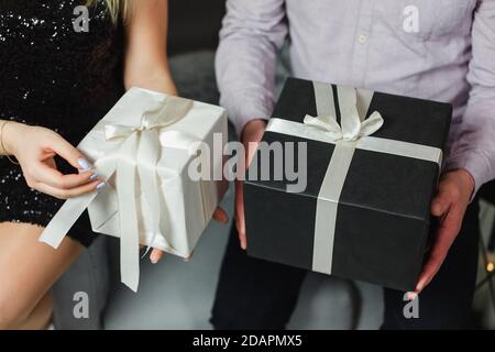 Weiße und schwarze Geschenkschachteln in männlichen und weiblichen Händen. Mann und Frau halten Geschenkschachteln mit Schleifen, Nahaufnahme. Paar schenken einander Geschenke. Hol Stockfoto