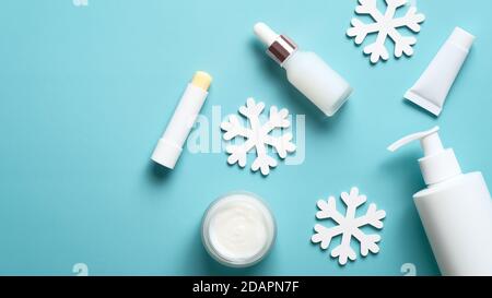 Winter Hautpflege Beauty-Produkte und Schneeflocken auf pastellblauem Hintergrund. Pumpflasche, Serum, Glas oder Creme, Lippenstift, Tube Verpackung Design. Flach liegend Stockfoto