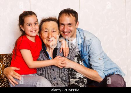 Die 95-jährige Frau und ihre Urenkelin schauen auf die Kamera. Sie sitzt auf einem Stuhl in ihrem Wohnzimmer. Stockfoto