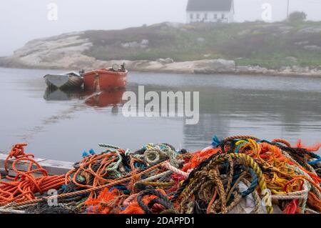 Orange und weiße Ruderboote verankert in Felsbucht mit Bündel von Angelausrüstung und Seil auf Dock im Vordergrund Umgeben von Nebel Stockfoto