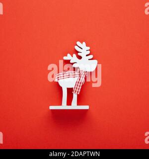 Weihnachtsdekoration, Spielzeug weißen Hirsch im karierten Schal auf rotem Hintergrund, kopieren Raum. Festliches Neujahrskonzept. Quadratisches, flaches Lay. Minimalistischer Stil. Oben Stockfoto