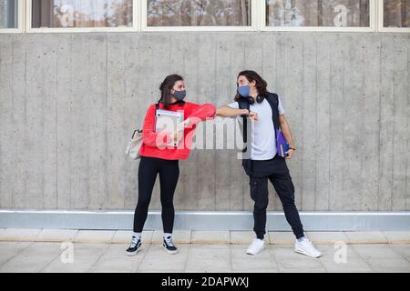 Zwei Universitätsstudenten stoßen ihre Ellbogen an, anstatt sich zu umarmen. Vermeiden Sie die Ausbreitung von Coronavirus, soziale Distanz. Stockfoto