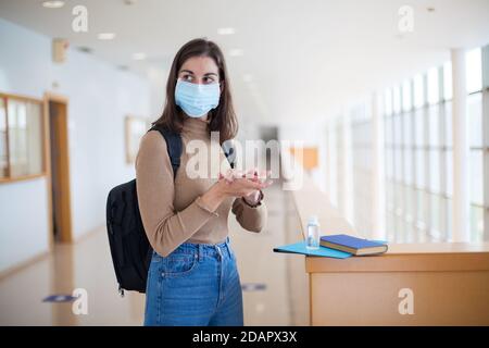 Junge Universitätsstudentin trägt Maske und verwendet Händedesinfektionsmittel Gel während covid-19 Stockfoto