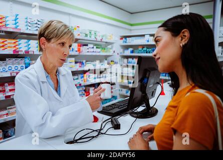 Leitende Chemikerin, die die Einnahme von Medikamenten berät, die verabreicht werden Junge Patientin über der Theke stehend in der Apotheke Stockfoto