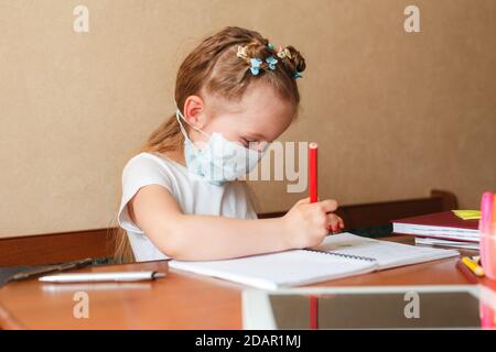 Nettes kleines Mädchen in Schutzmaske tun ihre Hausaufgaben zu Hause. Homeschooling während der Quarantäne. Stockfoto