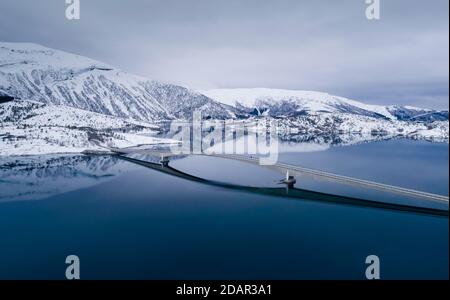 Lange Autobrücke über einen spiegelglatten blauen Fjord in einer Winterlandschaft, Gildeskal, Nordland, Norwegen Stockfoto