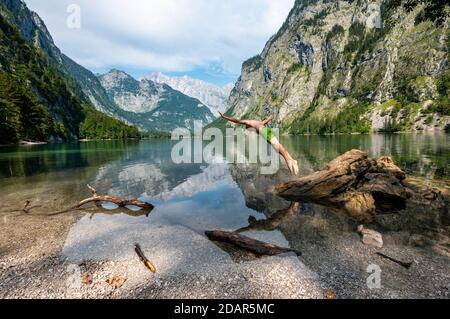 Junger Mann springt in den See, badet im Bergsee, Berge spiegeln sich im Obersee, hinter Watzmann, salet am Königssee, Berchtesgaden National Stockfoto