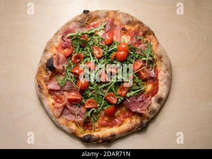 Italienische Pizza mit Tomatensauce, Mozzarella, Prosciutto, Rucola und Kirschtomaten, Draufsicht auf Holzhintergrund Stockfoto