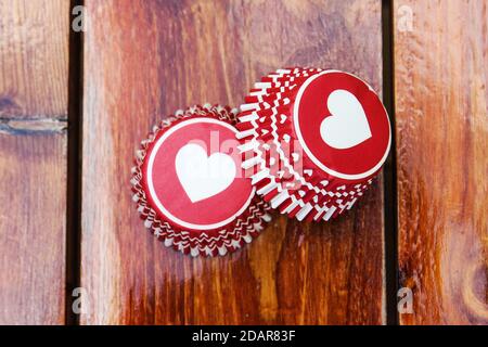 Rote Papier Cupcake Formen mit einem Herz Muster auf der hölzernen Arbeitsplatte. Foto des Produkts für Süßwarenläden. Stockfoto