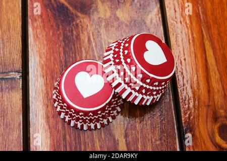 Rote Papier Cupcake Formen mit einem Herz Muster auf der hölzernen Arbeitsplatte. Foto des Produkts für Süßwarenläden. Stockfoto