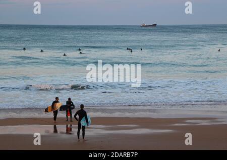 Drei Surfer bereit, am Strand in Sardinero zu surfen in der Abenddämmerung an einem milden Herbstabend verankerte Santander Cantabria Spanien Schiff Stockfoto