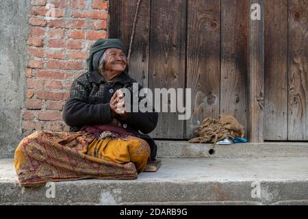 Freundliche lächelnde ältere Frau mit Kopftuch und Nasenring sitzt vor einer Holztür, Himalaya, Jiri, Khumbu Region, Nepal Stockfoto