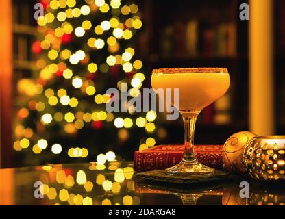Nahaufnahme von Chocolate Orange Martini - festlicher Weihnachtscocktail mit Weihnachtsdekoration, einem roten Buch und einer Kerze auf dem Tisch, Weihnachtsbaumbok Stockfoto