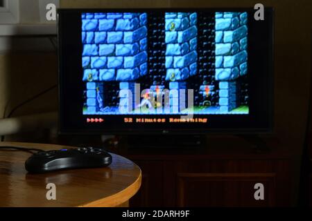 CHARKOW, UKRAINE - 12. NOVEMBER 2020: Sega Mega Drive Videospiel-Controller auf dem Tisch mit Prince of Persia Spiel auf großem Display Stockfoto