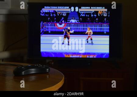 CHARKOV, UKRAINE - 12. NOVEMBER 2020: Sega Mega Drive Video Game Controller auf dem Tisch mit Wrestlemania Spiel auf großem Display Stockfoto