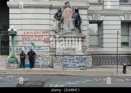 Zwei Polizisten, die eine Maske tragen, stehen am Eingang der Surrogate Hall of Records neben Graffitis und der vandalisierten Statue von Philip Martiny. Stockfoto