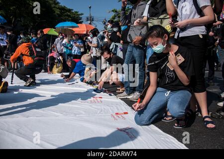 Bangkok, Thailand. November 2020. Demonstranten mit Gesichtsmasken schreiben während der Demonstration Botschaften auf ein riesiges Banner.Freie-Kunst-Aktivisten protestieren bei einem Mob-Festival vor dem Demokratiedenkmal und fordern den Rücktritt von Thailands Premierminister Prayuth Chan-ocha, einen Entwurf einer neuen Verfassung und Reformen der Monarchie. Kredit: SOPA Images Limited/Alamy Live Nachrichten Stockfoto