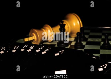 Darstellung eines Kartenstapel mit schwarzen Karten, die nur Diamantkarten zeigen, auf einem Schachbrett mit vier stehenden Schachfiguren und einem großen gelben König, der sich hinlegt. Stockfoto
