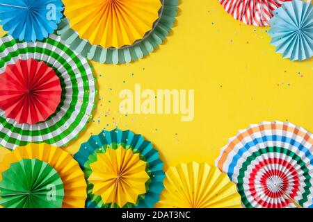 Mehrfarbige Papierrosetten in verschiedenen Größen auf gelbem Hintergrund. Dekoration und Dekoration für Party, Geburtstag oder Urlaub. Stockfoto