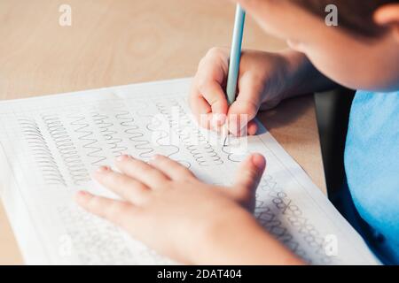 Nahaufnahme von Schuljunge tun Schreiben Aufgabe. Vorschreiben Übung, um die Hand für Schreiben Briefe vorzubereiten. Konzept der Kindererziehung Stockfoto