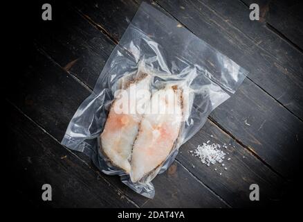 Tiefgefrorene grönländische Heilbutt-Steaks vakuumverpackt auf dem Holzschneidebrett. Nahaufnahme. Stockfoto