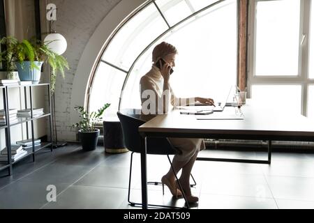 Selbstbewusste Geschäftsfrau, die am Telefon spricht und am Schreibtisch im Büro sitzt Stockfoto