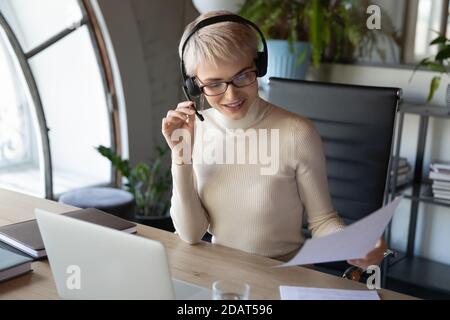 Lächelnde Geschäftsfrau trägt Headset Arbeiten mit Dokumenten, Kundenberatung Stockfoto