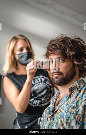 Aufnahme eines Friseurs in einer medizinischen Maske, der sie tut Job - Neue normale Stockfoto