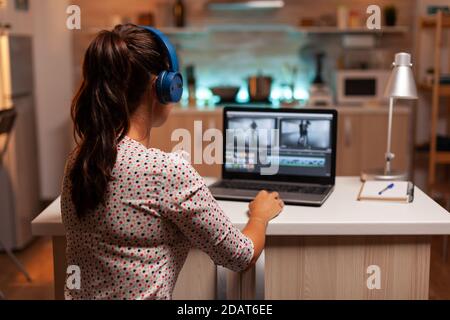 Video-Editor arbeitet an einem Projekt aus der Küche zu Hause in der Nacht Zeit und Musik auf Kopfhörer hören. Content Creator zu Hause arbeiten an Montage von Film mit moderner Software für die Bearbeitung. Stockfoto
