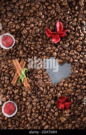 Kaffeebohnen auf einem Kaffeebohnen Hintergrund mit roten Blumen, roter Schokolade und Zimt. Espresso am Morgen. Kaffeetasse. Stockfoto